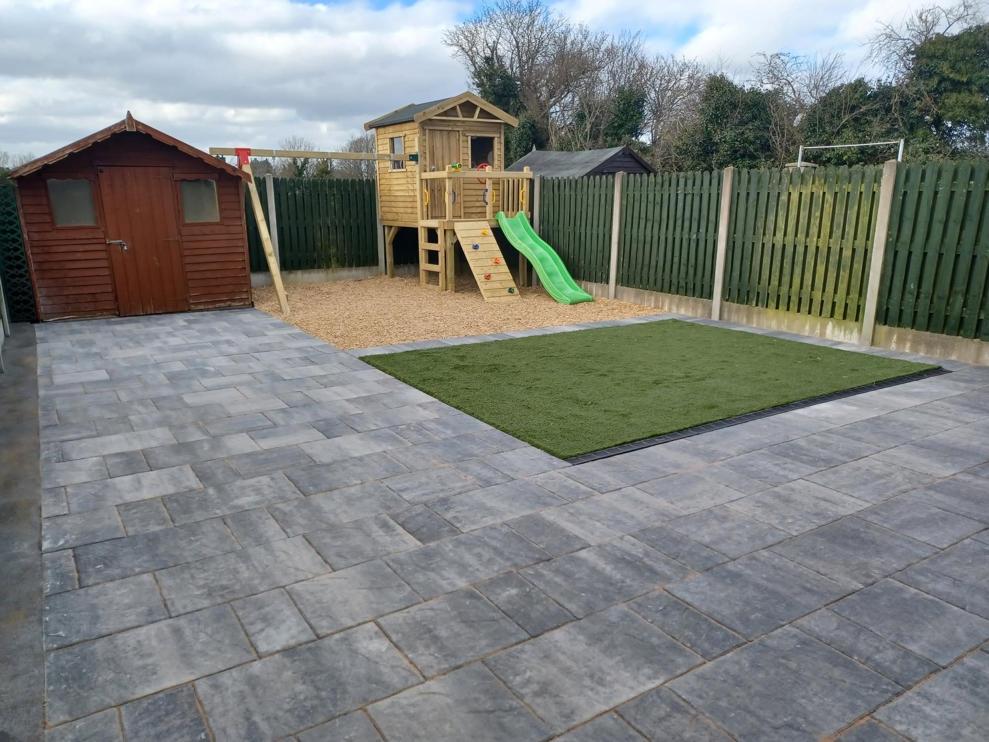 Charcoal paving with playhouse, artificial lawn and bark area in a Laois back garden
